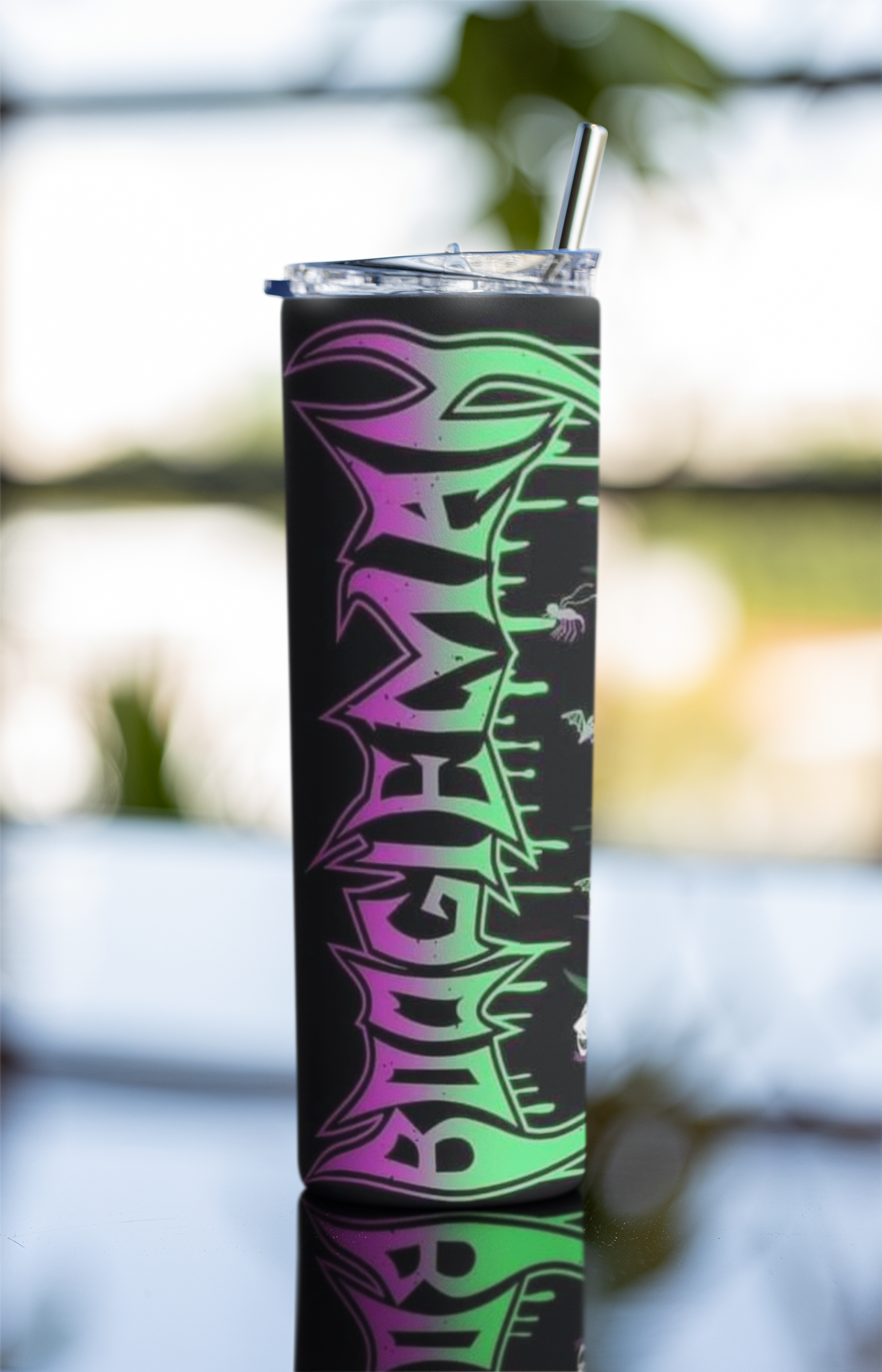 Tumbler with colorful design and straw against a blurred natural background
